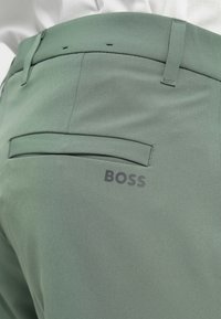 Light green trousers made of smooth fabric, featuring a back pocket and a subtle printed "BOSS" logo. Design includes a tailored fit and belt loops.