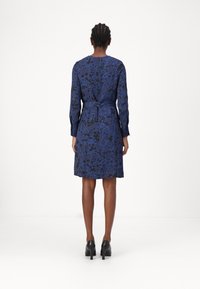 Marinblå blommig klänning med långa ärmar, åtsittande midja och rakt skär. Har ett kontrasterande blått blommönster och en rund halsringning.