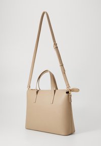 Beige synthetic handbag with two top handles and a detachable, adjustable shoulder strap. Smooth texture with gold-tone hardware accents.