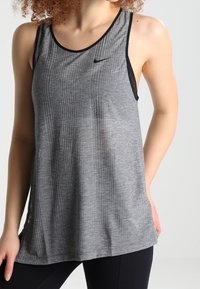 Grijze, geribbelde atletische tanktop met zwarte bies en Nike-logo op de borst; lichtgewicht stof met een ontspannen pasvorm.