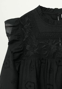 Robe noire avec col et manches à volants, ornée de dentelle florale et de broderie de perles sur le corsage, avec des découpes florales à œillets sur la jupe.