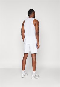 Canotta bianca senza maniche e pantaloni corti, taglio atletico, abbinati a sneaker grigie. Design minimal con accenti del logo e bande laterali sui pantaloni.