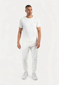 Hvid T-shirt med korte ærmer og rund hals, kombineret med matchende hvide joggingbukser og hvide sneakers. Glat tekstur og tætsiddende design.