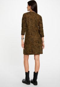 Bruin luipaardprint jurk met lange mouwen en een ontspannen pasvorm, gemaakt van zachte stof, gecombineerd met zwarte stevige enkellaarsjes.