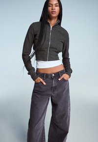 Maglione grigio scuro con zip, maniche lunghe, abbinato a jeans neri sbiaditi e morbidi con dettagli laterali. Tessitura liscia.