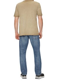 Chemise kaki à manches courtes, jean en denim bleu avec une texture décolorée, et baskets noires avec des accents blancs, vues de dos.