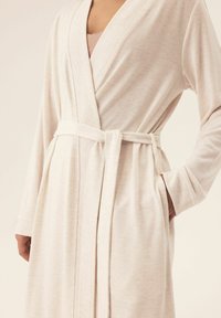 Jasno beżowy szlafrok wykonany z miękkiego, prążkowanego materiału. Posiada fason w formie owijanej, długie rękawy, pasek oraz kieszenie po bokach.