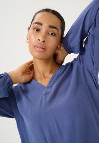 V-hals, langetermijnshirt van gestructureerde, diepblauwe stof. Kenmerkt zich door een subtiele stiksel en een losse pasvorm. Verfraaid met een lichte glans.