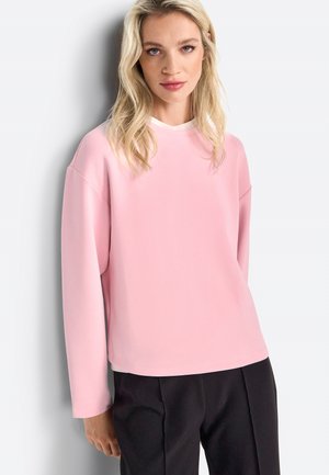 Lichtroze sweatshirt met een ronde hals en lange mouwen, voorzien van een gestructureerde stof en een relaxte pasvorm. Gecombineerd met zwarte broek.
