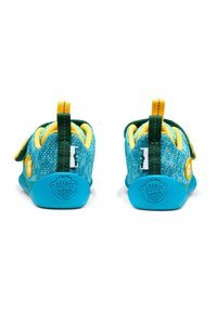Scarpe per bambini turchesi con tomaia in tessuto, dettagli gialli, linguetta verde sul tallone, cinturino in velcro e suola in gomma con un dettaglio del logo.