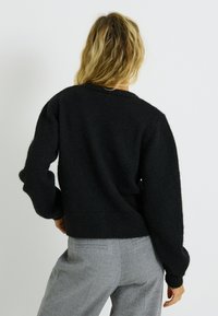 Pull en tricot noir avec une coupe décontractée, un col rond et un ourlet côtelé. Il présente des manches longues légèrement bouffantes et une texture douce.