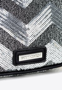 Zwart en zilver paillettendoek met een chevronpatroon, voorzien van een zwarte leren accent en een metallic label met "WITTCHEN."