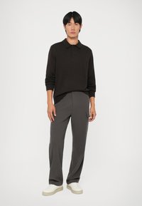 Polo de punto marrón oscuro con cuello, tres botones y puños acanalados, combinado con pantalones gris sueltos y zapatillas blancas.