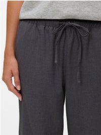 Nærbilde av en person som har på seg mørkegrå joggebukser og en lysegrå topp, med venstre hånd hvilende ved siden av buksene.