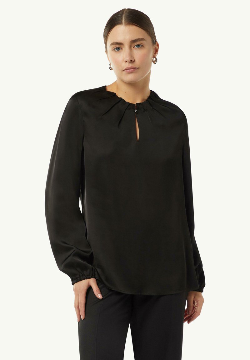 Schwarze Satinbluse mit einem Schlüssellochausschnitt, sanften Rüschen am Kragen und langen Ärmeln mit elastischen Bündchen. Glatte, glänzende Textur.