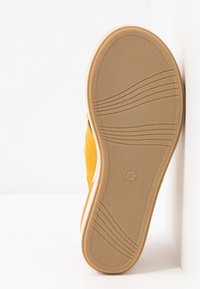 Chaussure jaune en daim à enfiler avec une semelle extérieure en caoutchouc texturé. La semelle plate présente des motifs en vagues et une étiquette de taille (37) au fond.