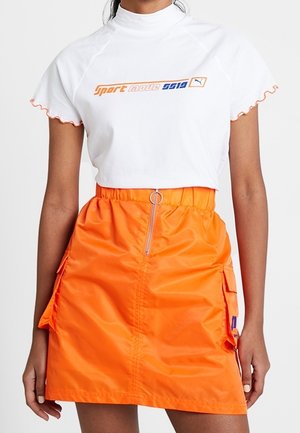 Biały krótki t-shirt z tekstem "sport magic 9919" w kolorach pomarańczowym i niebieskim, połączony z jaskrawo pomarańczową spódnicą na zamek z bocznymi kieszeniami.