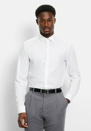 White long-sleeve button-up shirt with a collar, paired with gray pleated trousers and a black belt. Smooth fabric, classic fit.