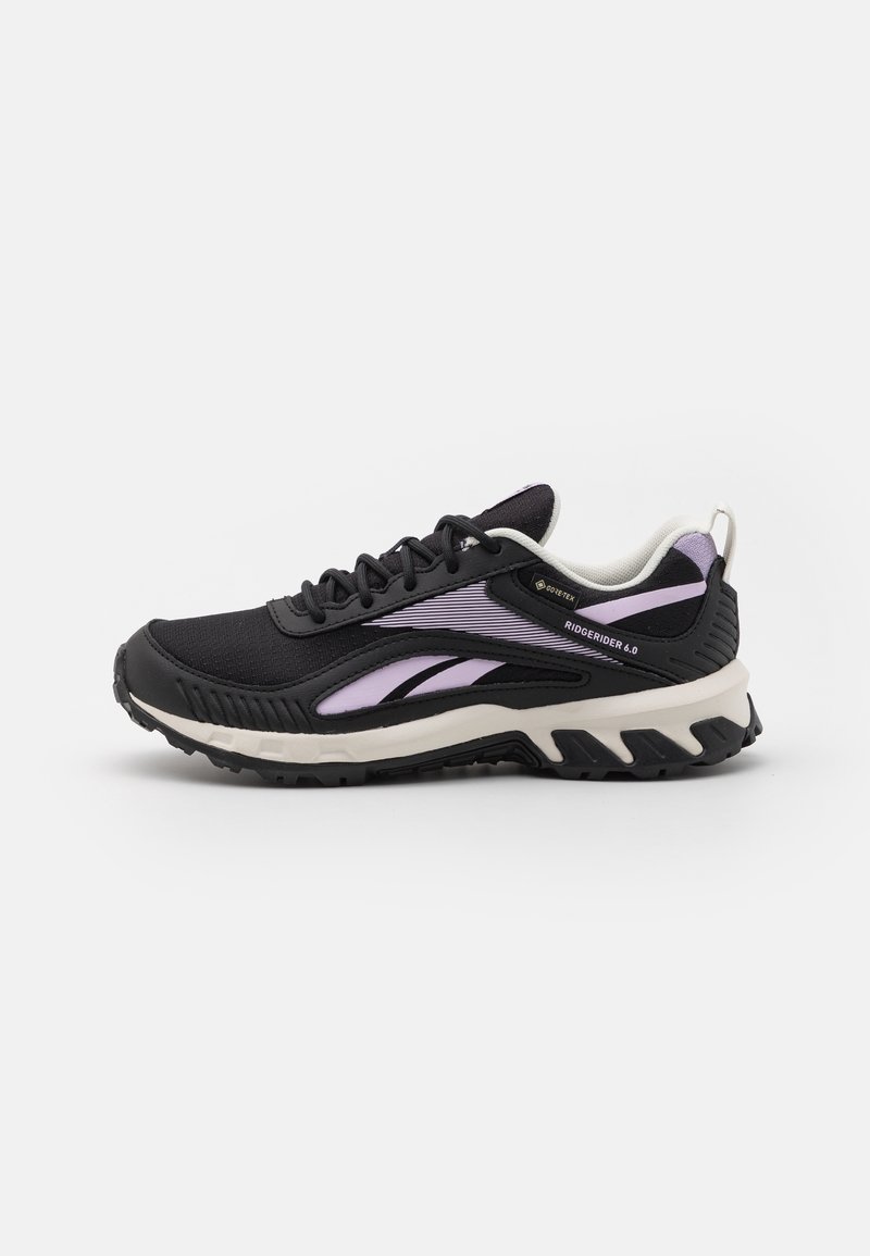 Baskets basses Reebok Ridgerider 6.0 noires et lavande avec semelle blanche et semelle robuste, conçues pour un usage extérieur.