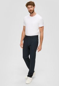 Dunkelblaue Hose mit geradem Schnitt, flacher Vorderseite, Gürtelschlaufen und einem kleinen Logo-Detail, kombiniert mit einem schlichten weißen T-Shirt und Sneakern.