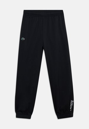 Pantalon noir à taille élastique avec poignets aux chevilles, avec un petit logo crocodile vert sur la cuisse gauche et le texte blanc Lacoste sur le poignet de la jambe droite.