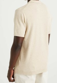 Beige stickad pikétröja med kort ärm som har en ribbad krage, texturerade axelsömmar och sidoflikar för ökad komfort.