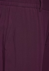 Pantalons violet foncé fabriqués en matériau doux, dotés d'une taille élastique et de poches latérales. Le tissu a une texture lisse avec un minimum de couture.