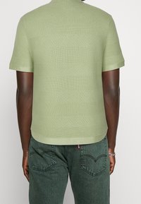 Koszulka polo z krótkim rękawem w jasnym zielonym kolorze z teksturowanymi paskami. Posiada klasyczny kołnierzyk i prosty krój. W komplecie z ciemnozielonymi dżinsami.