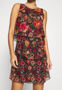 Robe sans manches en tissu noir transparent avec un design superposé. Présente des fleurs rouges, roses et jaunes vives. Légère et fluide.