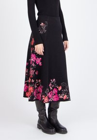 Gonna nera a fiori con ricami rosa e arancioni lungo l'orlo, realizzata in un tessuto texturizzato. Indossata con stivali neri al ginocchio.