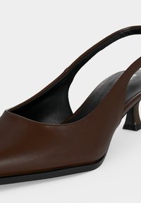 Chaussure slingback en cuir marron avec bout pointu et petit talon courbé, semelle noire, présentée sur fond blanc.