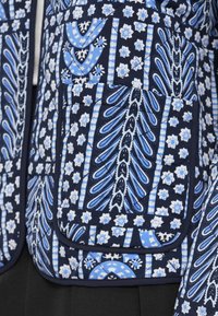 Καπιτονέ μπουφάν με βάση σε ναυτικό μπλε χρώμα και μπλε ανθικά και γεωμετρικά μοτίβα, που περιλαμβάνει τσέπη με πατς και αντιθετικές λεπτομέρειες στο τελείωμα.