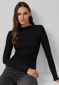 Zwarte top met lange mouwen, ribbelstructuur en kleine stippenpatronen. Beschikt over een scalloped halslijn en zoom, gemaakt van rekbare stof.