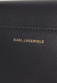Juodas odinis piniginė su tekstūruota danga ir auksiniu "KARL LAGERFELD" logotipu išspaudytu paviršiuje. Paprastas, elegantiškas dizainas.