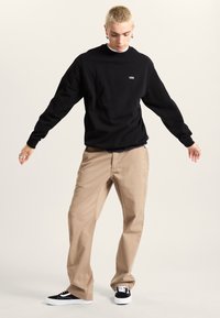 Black sweatshirt with a Vans logo, beige pants, and black sneakers with white soles. The outfit has a casual streetwear style.