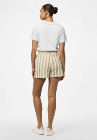 T-shirt blanc à manches courtes, associé à un short rayé beige et crème. Modèle portant des baskets claires, vu de dos.