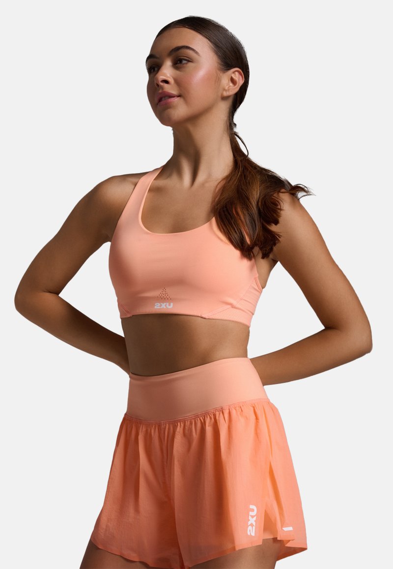 Perzikkleurige sportbeha met logo, voorzien van een zachte stof en brede banden, gecombineerd met bijpassende high-waisted shorts met een uitlopende ontwerp en logoaccent.