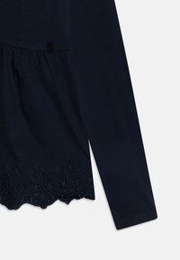 Marinblå bomullströja med lång ärm, samlad midja och scalloped nederkant med blommönsterbroderi vid botten.