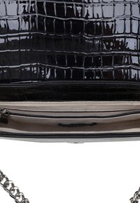 Sac à main en cuir verni noir avec texture crocodile, bandoulière en chaîne argentée et poche intérieure zippée. Doublure intérieure lisse.