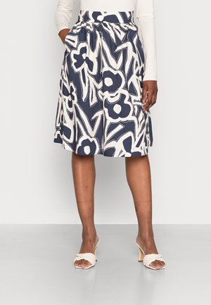 Granatowa i biała spódnica do kolan z wyrazistym abstrakcyjnym wzorem kwiatowym, zestawiona z białymi plecionymi sandałami na obcasie oraz białą bluzką z długim rękawem.