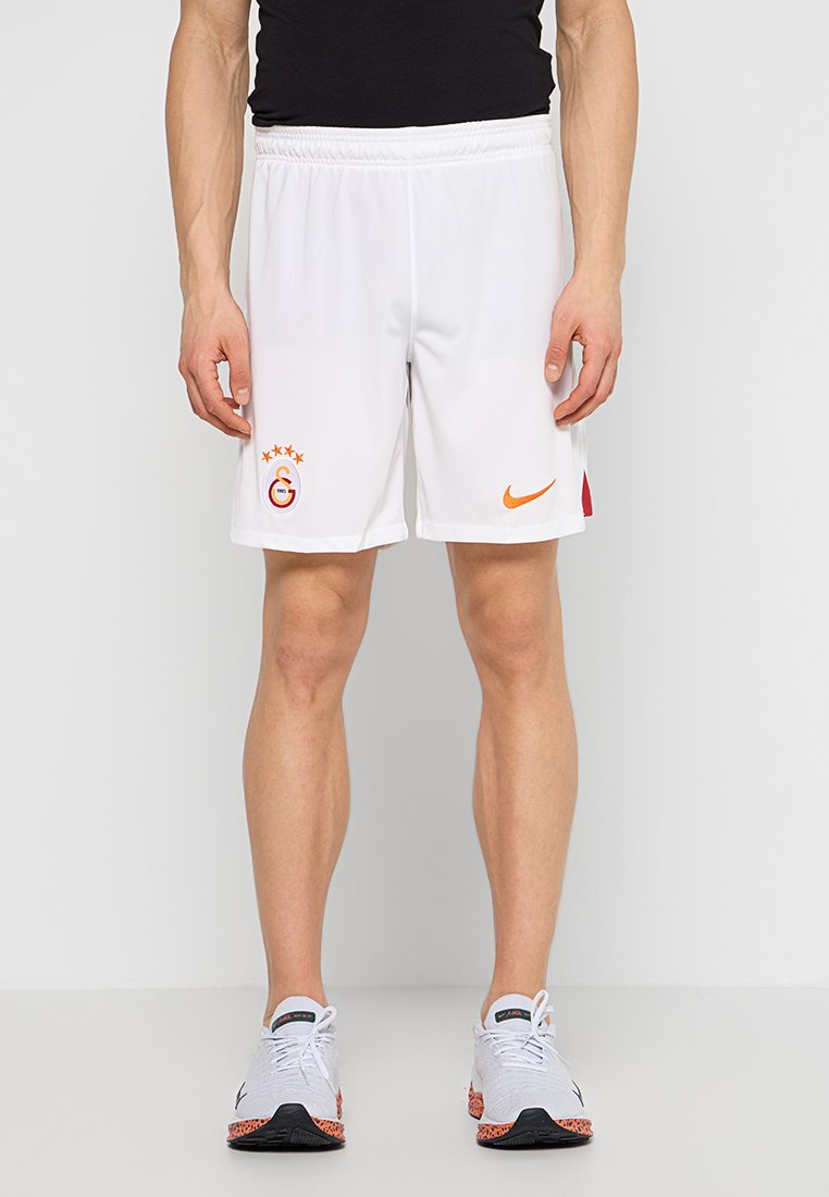 Białe sportowe spodenki z elastycznym paskiem w talii, z pomarańczowym logotypem Nike i emblematem drużyny z trzema gwiazdkami z boku.