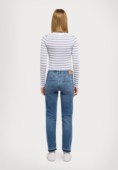Bluza cu mânecă lungă, cu dungi gri și albe, asociată cu blugi din denim albastru. Blugii au o croială clasică și buzunare la spate.