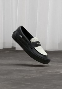 Schwarzer Leder Slipper mit einem weißen strukturierten Panel, runder Spitze und flacher Gummisohle. Verfügt über einen dekorativen Riemen über dem Obermaterial.