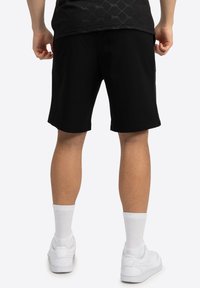 Sorte bomuldsshorts med en afslappet pasform, der har en glat tekstur. Bæret med hvide sneakers og sokker i ankel-længde.
