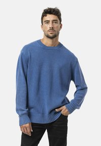 Blauwe gebreide trui met een geribde ronde hals en manchetten. De stof heeft een gestructureerde afwerking en de silhoe t is relaxed-fit. Draag het over zwarte jeans.