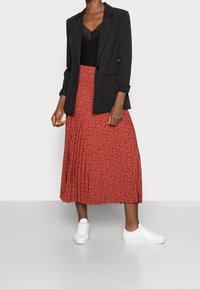 Svart blazer med uppvikt ärm, lager över en svart topp med spetsdetaljer. Röd midiklänning med svart blommönster, ihop med vita sneakers.