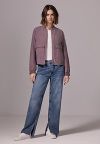 Bomberjacka i dämpad mauve, med två bröstfickor och elastiska ärmslut. Matchad med vida slitna jeans och vita sneakers.