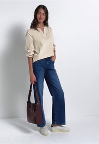 Ecrufarbenes Langarmhemd mit Kragen, kombiniert mit blauen, weiten Jeans. Eine braune Handtasche und weiße Sneaker vervollständigen das Outfit.