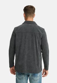 Grå kordfløjl skjortejakke med krave, lange ærmer og en tekstureret stofoverflade, der har et lige rygdesign.