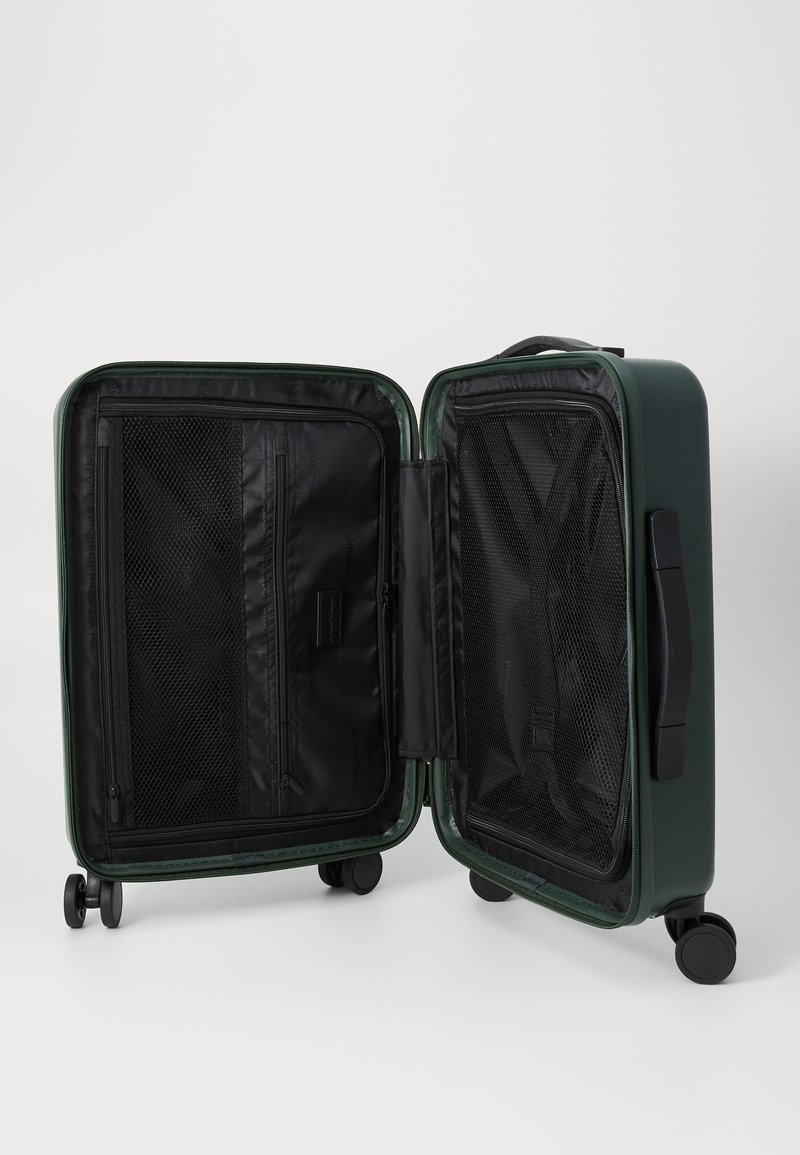 Maleta de hard-shell en color verde oscuro con interior negro. Cuenta con dobles compartimentos, bolsillos de malla y ruedas de fácil rodaje.